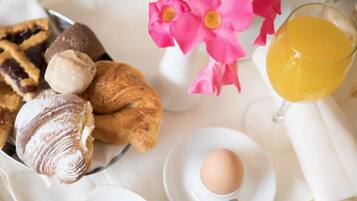 A breakfast setting with pastries, a glass of orange juice, and a flower arrangement.