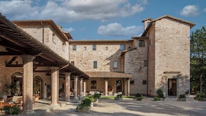Un patio con edificios de piedra, mobiliario exterior y una zona cubierta con columnas.