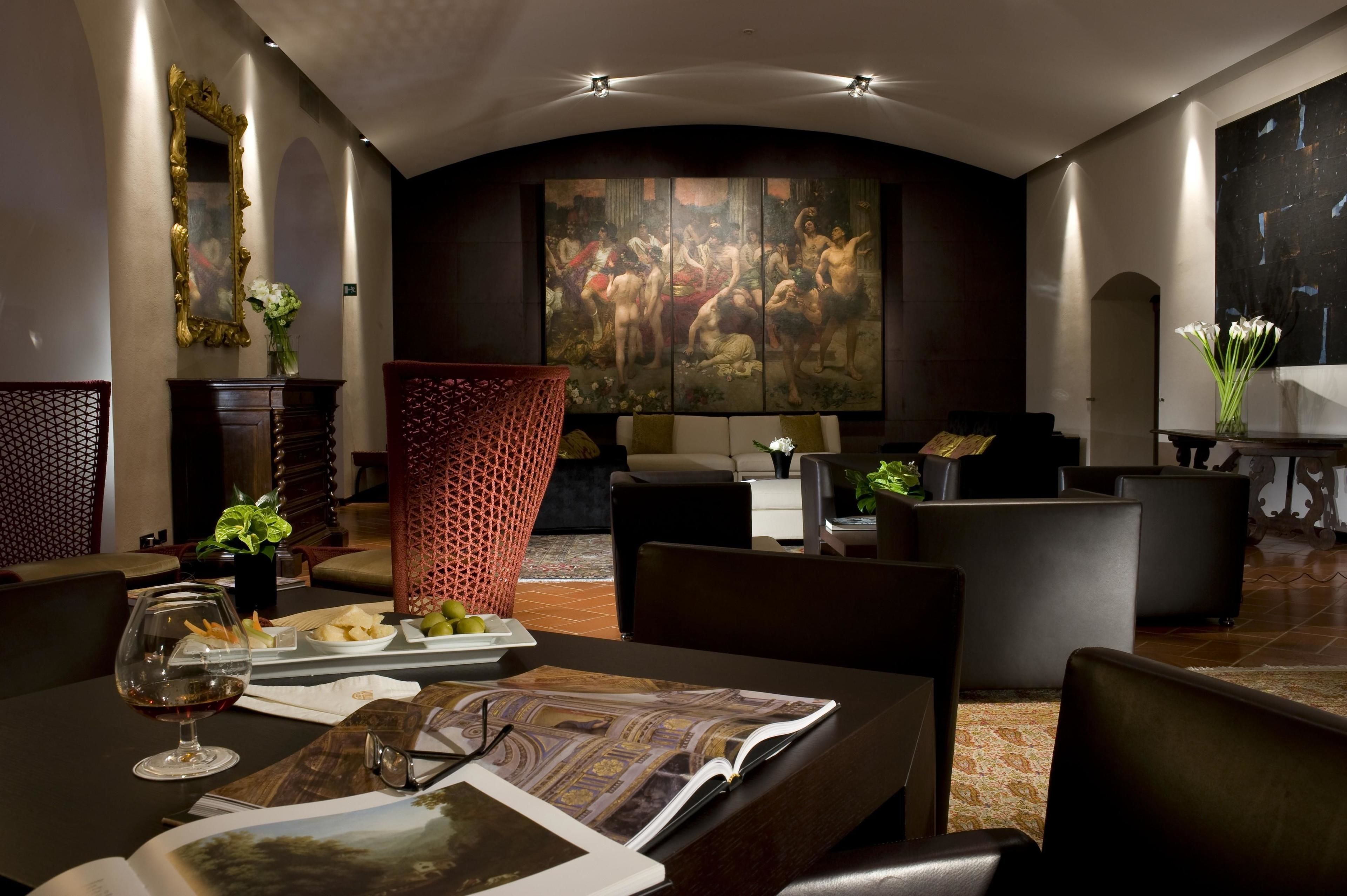 Un hall d’hôtel moderne, agrémenté d’un grand tableau classique, de sièges confortables et d’un espace repas avec un verre à vin et un menu.