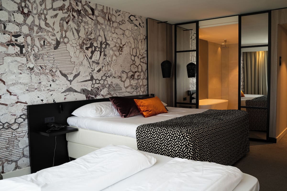Een moderne hotelkamer met een groot bed, een nachtkastje met een telefoon en een kamerhoog hoofdbord met een patroon.