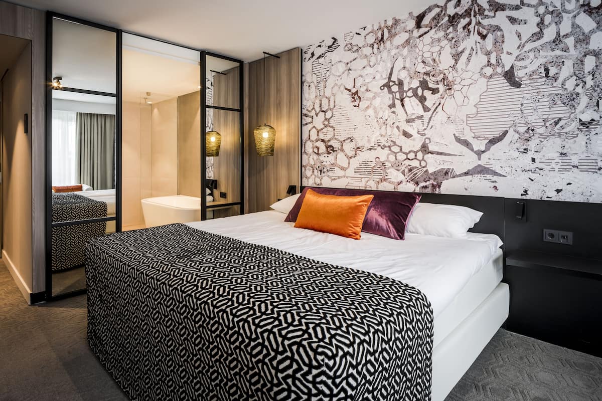 Een moderne hotelkamer met een groot bed, een badkamer met een bad, en een muur met een abstract ontwerp.