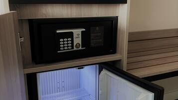 A compact refrigerator with a digital lock and card reader, a coffee maker, and a kettle on a wooden shelf above it.