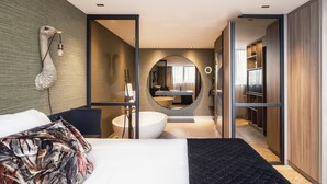 Ein modernes Hotelzimmer mit einem großen Bett, einem runden Spiegel, einer integrierten Badewanne und einem begehbaren Kleiderschrank.