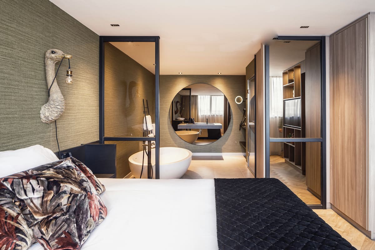 Een moderne hotelkamer met een groot bed, een ronde spiegel, een inloopbad en een inloopkast.