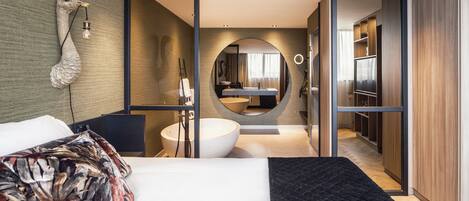 Una habitación de hotel moderna con una cama grande, un espejo redondo, una bañera empotrada y un vestidor.