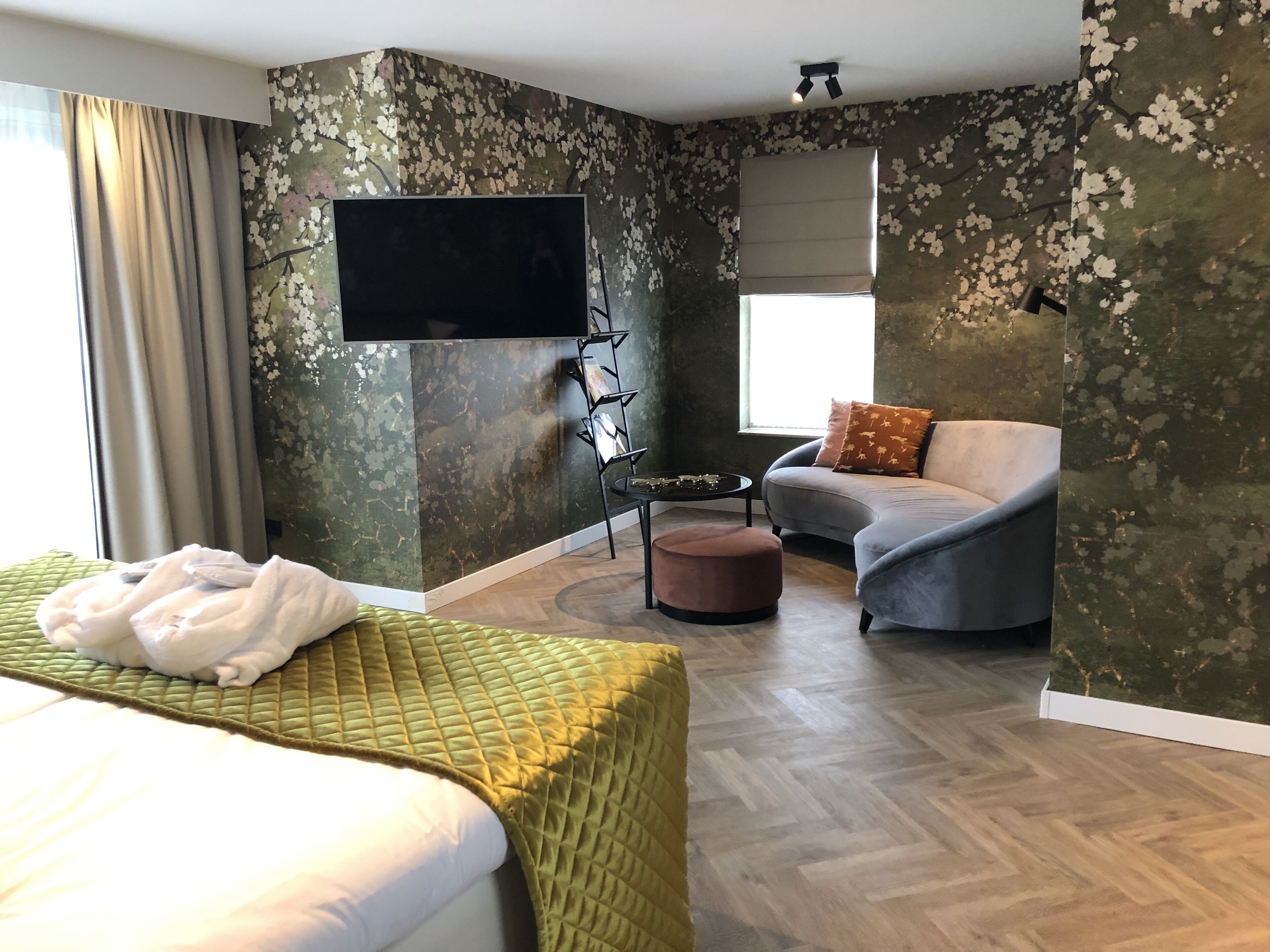 Een hotelkamer met een bed, een slaapbank, een aan de muur bevestigde televisie, een tafeltje en een raam met gordijnen.