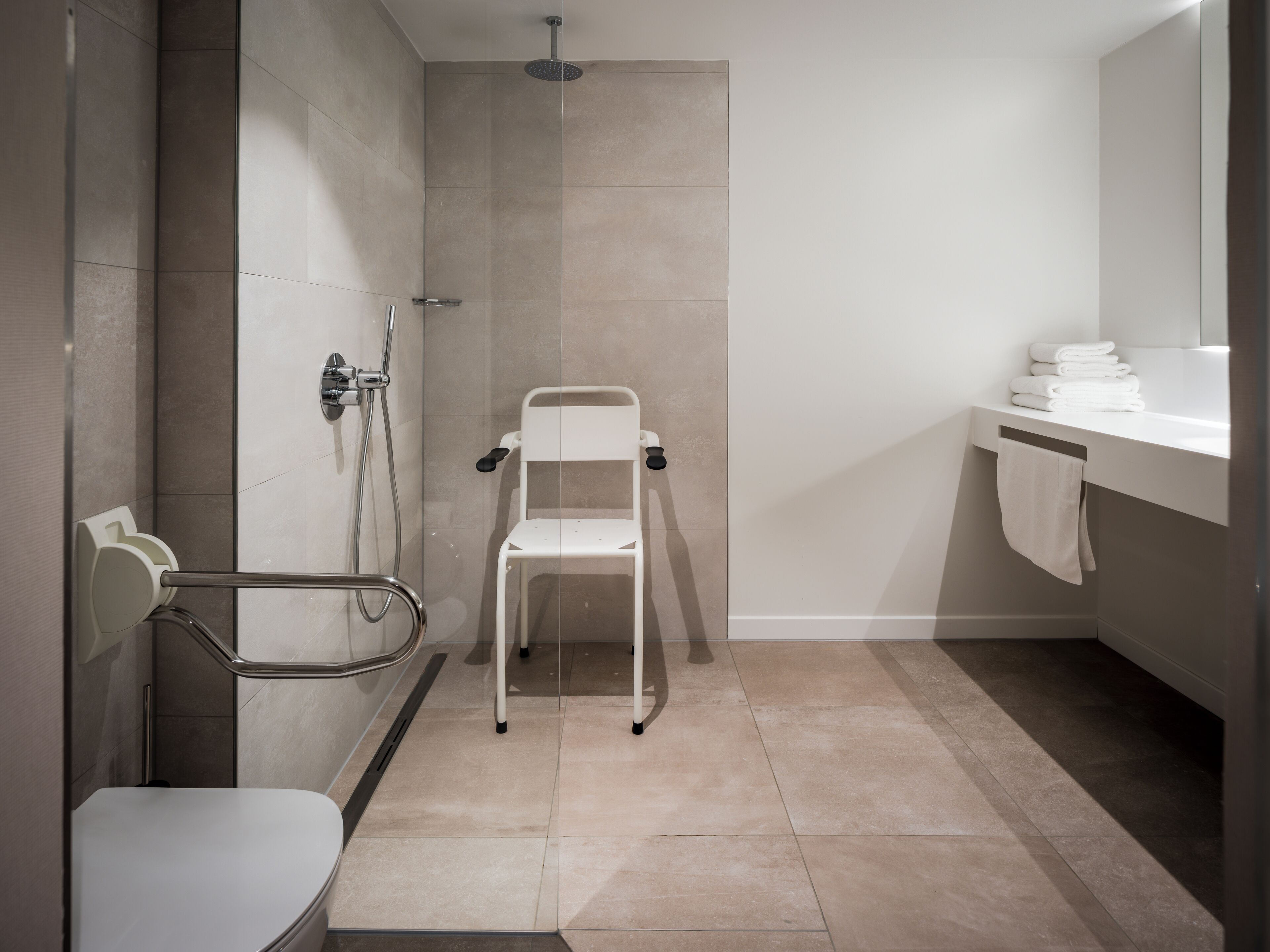 Een moderne badkamer met douche, toilet en een stoel.