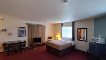 A hotel room with a bed, a desk, a television, a lamp, and a microwave.