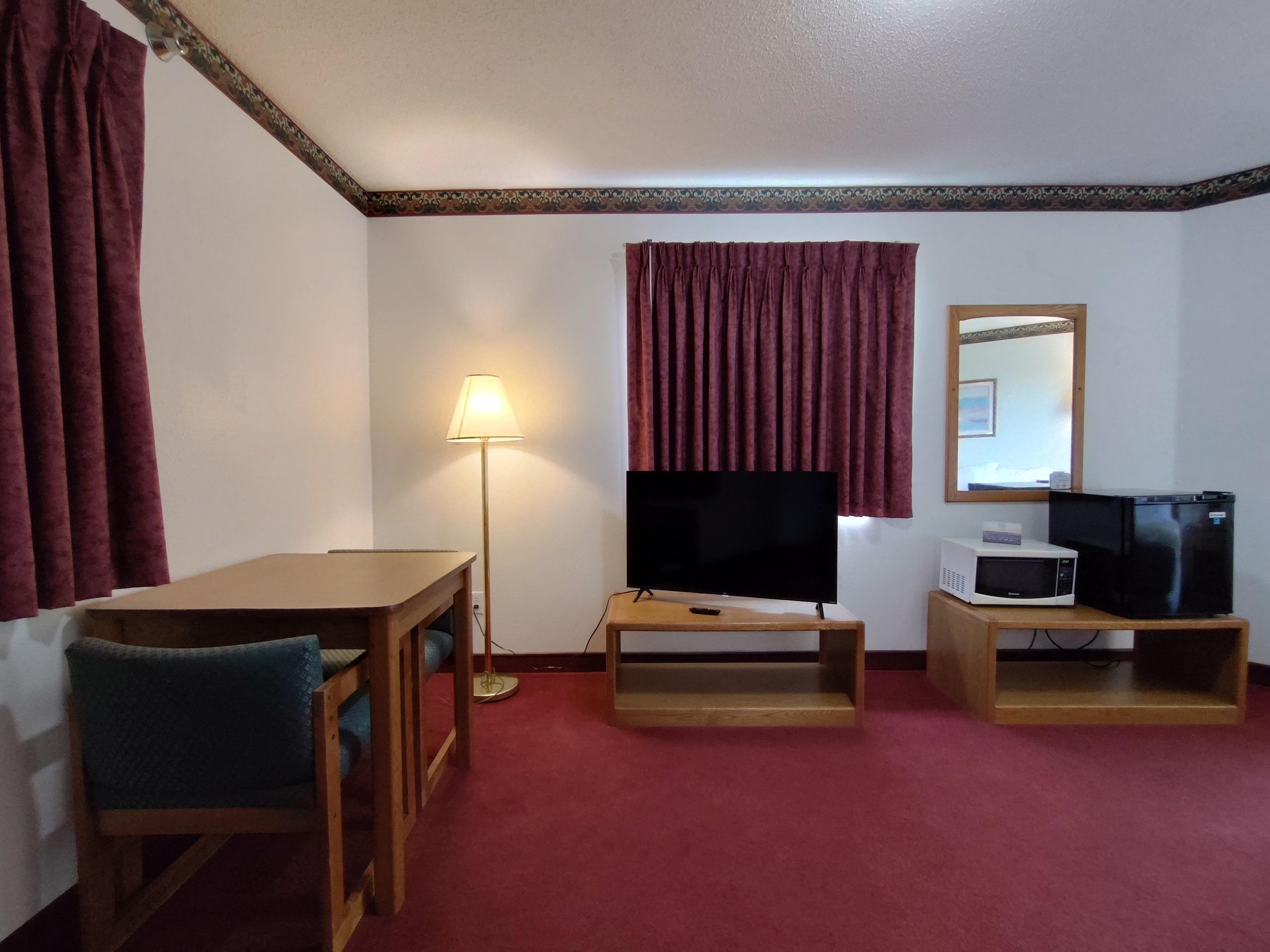 Habitación de hotel con un escritorio de madera, televisor, microondas y un espejo en la pared.