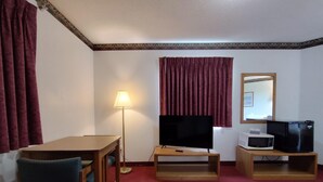 A hotel room with a wooden desk, a television, a microwave, and a mirror on the wall.