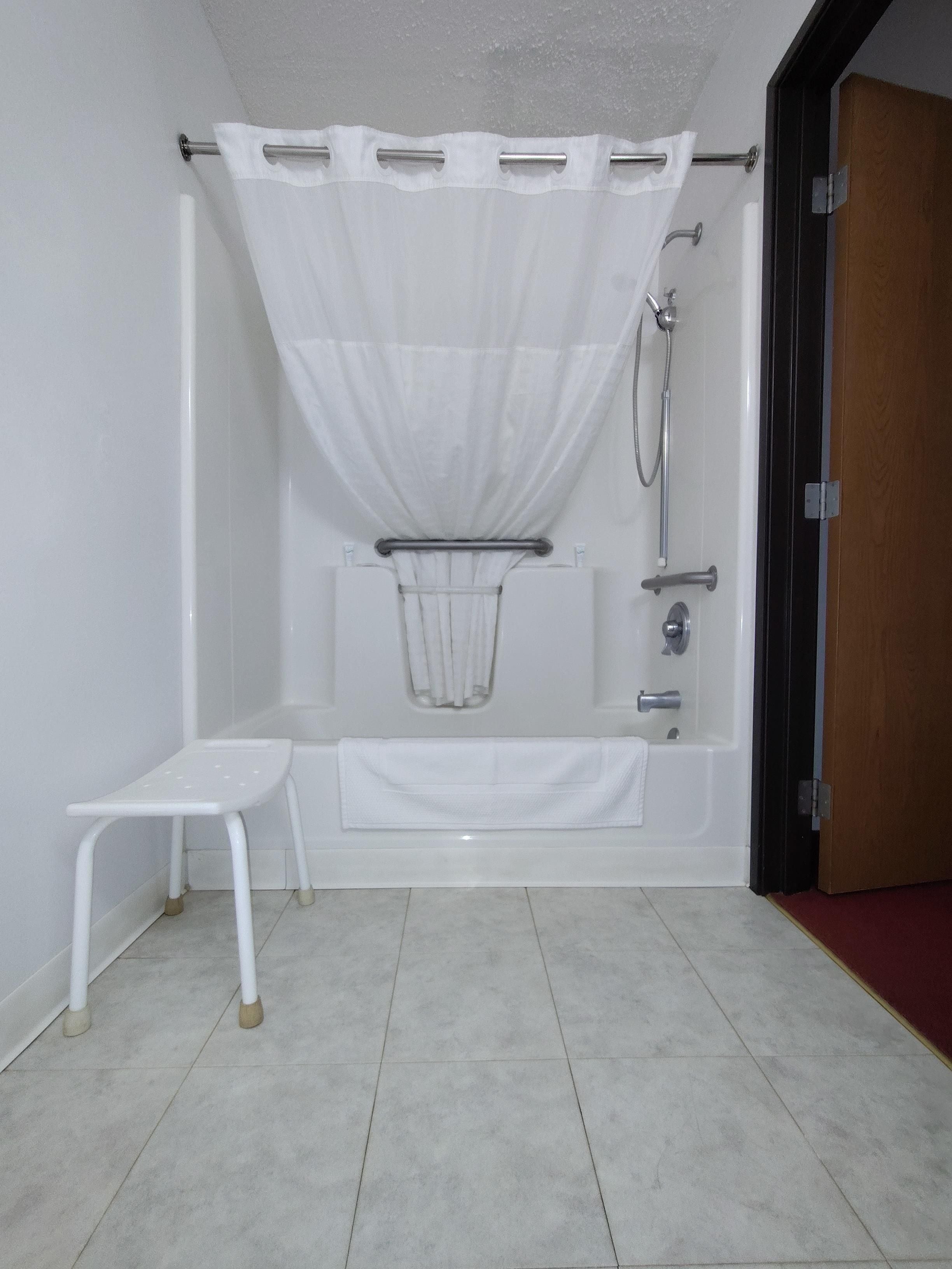 Un baño con bañera, ducha, toallero blanco y un taburete pequeño.
