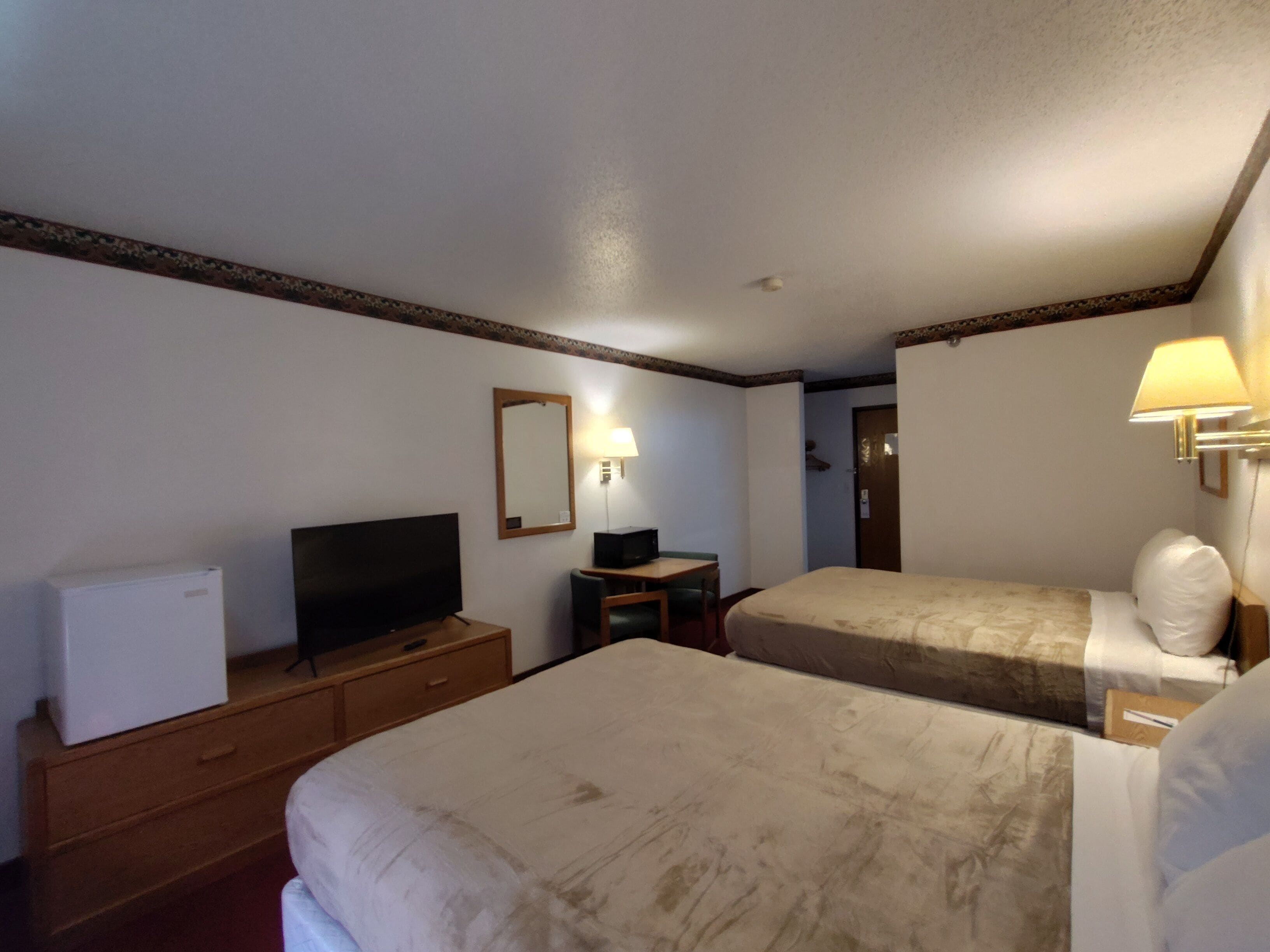 A hotel room with two beds, a television, a desk, and a lamp.
