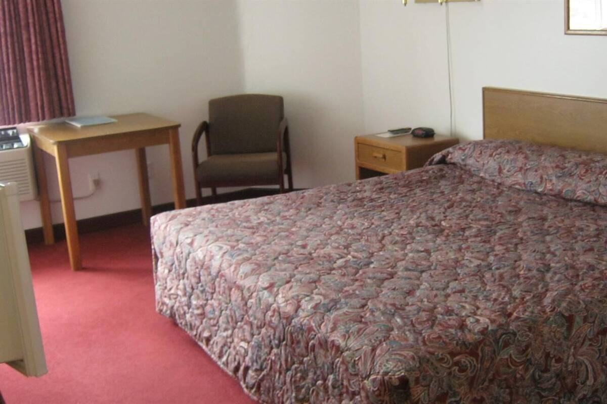 A hotel room with a bed, a desk, a chair, and a nightstand.