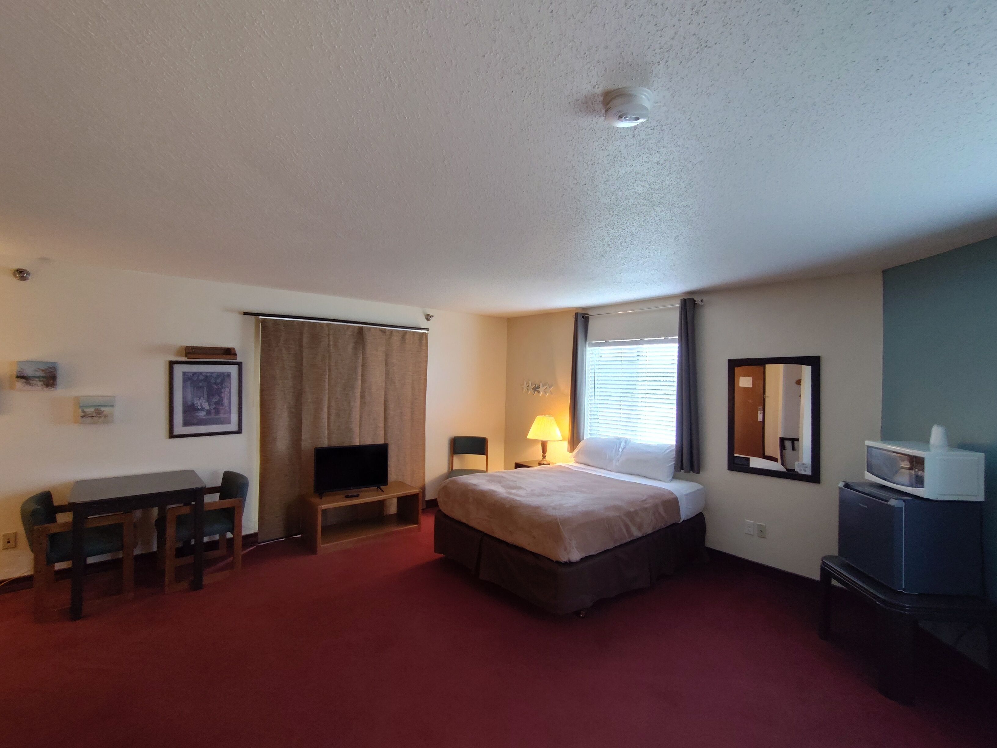 A hotel room with a bed, a desk, a television, a lamp, and a microwave.