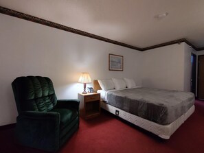 A bedroom with a single bed, a nightstand with a lamp, a green armchair, and a painting on the wall. - Americas Best Value Inn & Suites Clear Lake (Clear Lake)