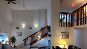 A spacious living area with a staircase, seating arrangements, and a television.