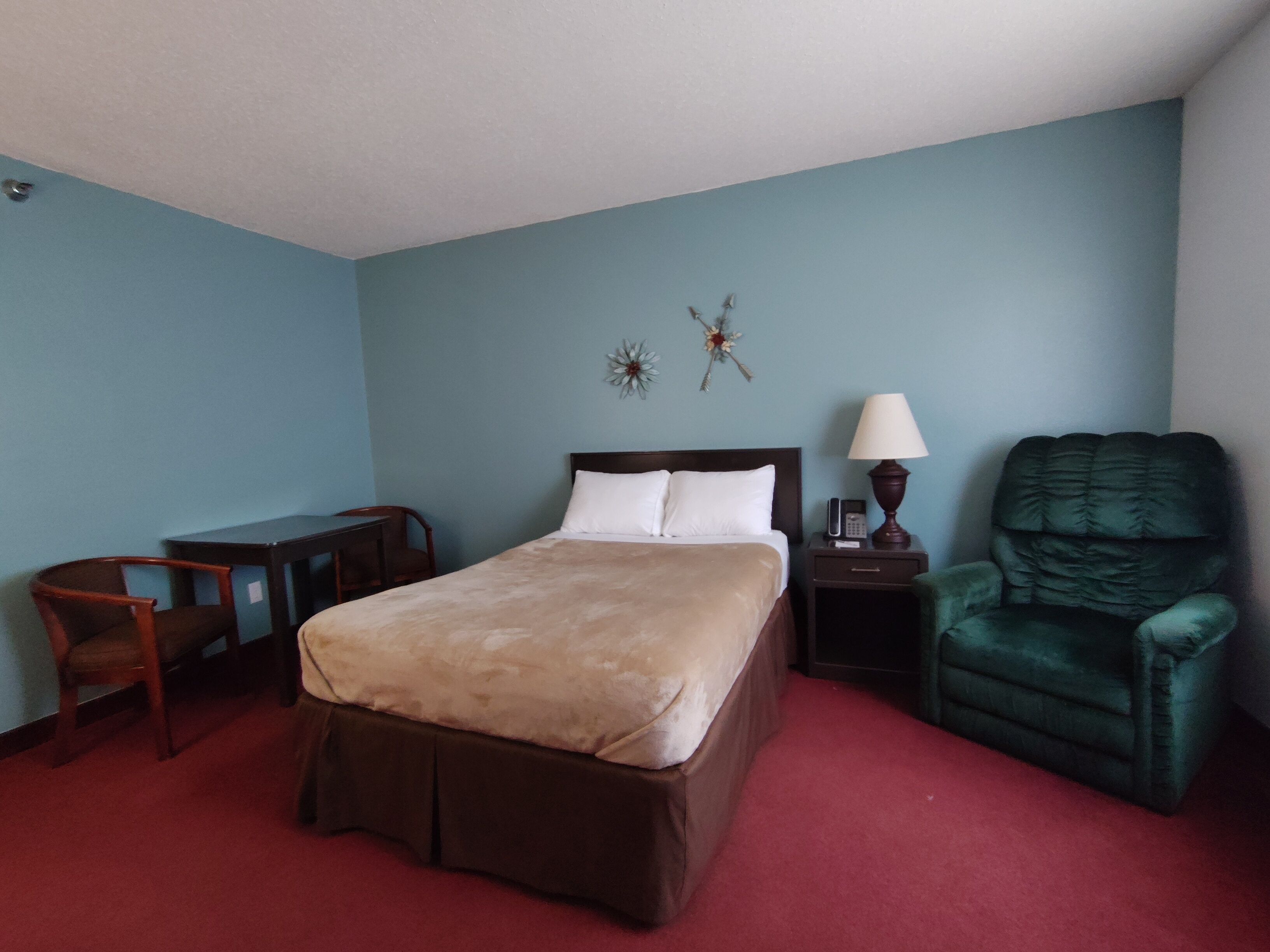 Una habitación de hotel con cama, escritorio, silla, lámpara y un sillón verde.