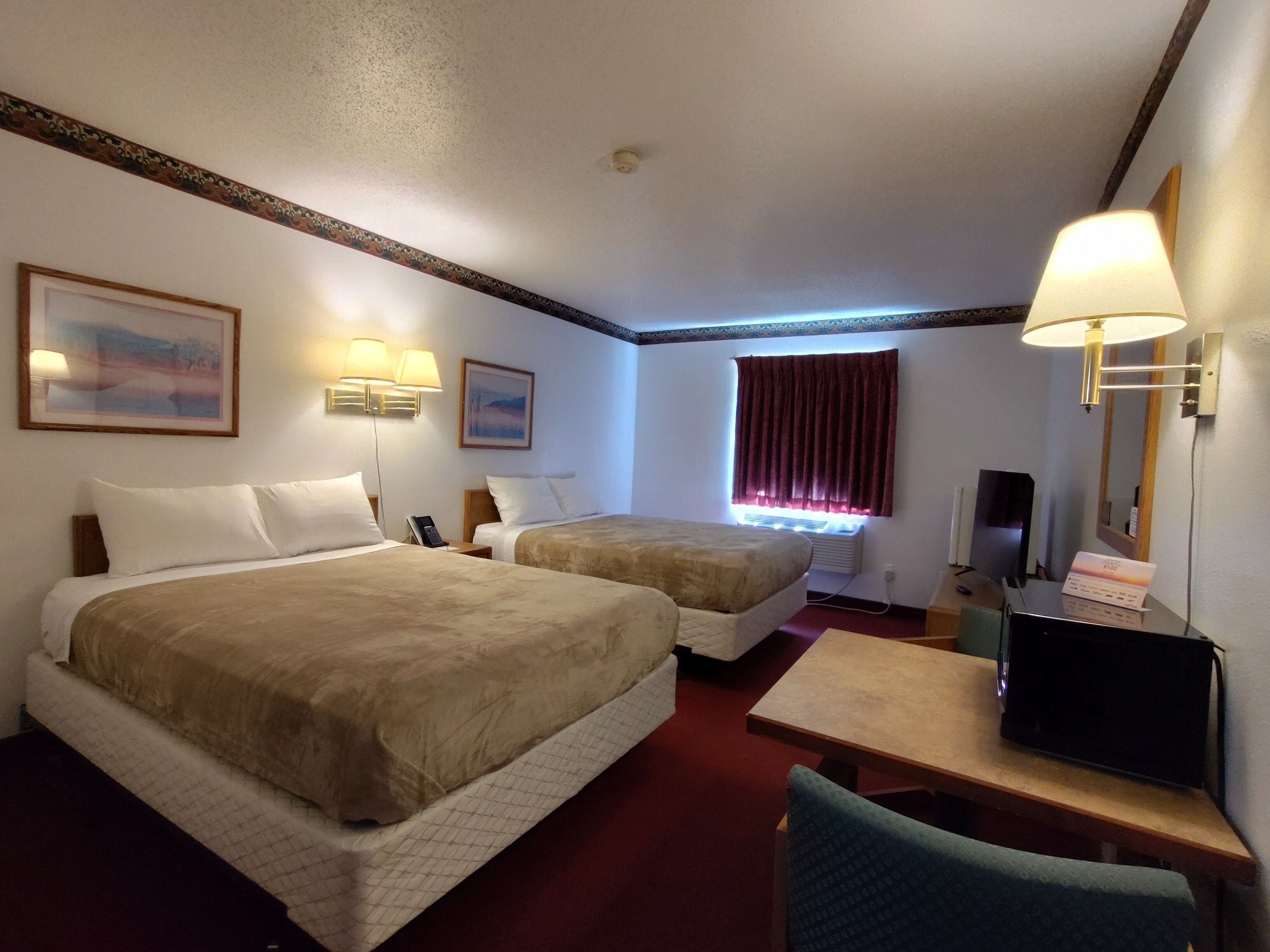 A hotel room with two beds, a desk, a chair, a television, and a window with curtains.