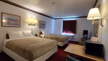 A hotel room with two beds, a desk, a chair, a television, and a window with curtains.