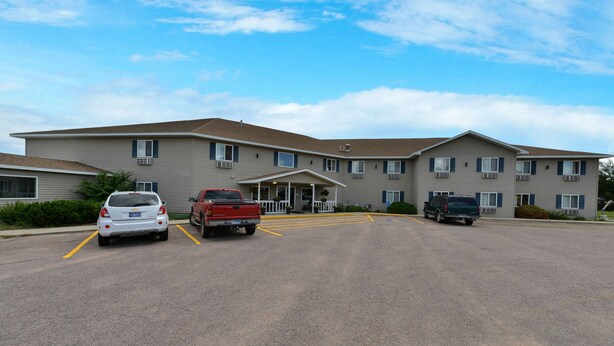 A multi-story hotel with a central entrance, parking lot, and several vehicles parked. - Americas Best Value Inn & Suites Clear Lake (Clear Lake)