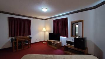 Une chambre d’hôtel équipée d’un lit, d’un bureau, d’une chaise, d’une télévision, d’une lampe et d’un miroir.