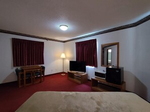 Une chambre d’hôtel équipée d’un lit, d’un bureau, d’une chaise, d’une télévision, d’une lampe et d’un miroir.