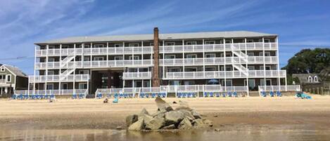 A multi-story hotel with balconies, located near a beach.