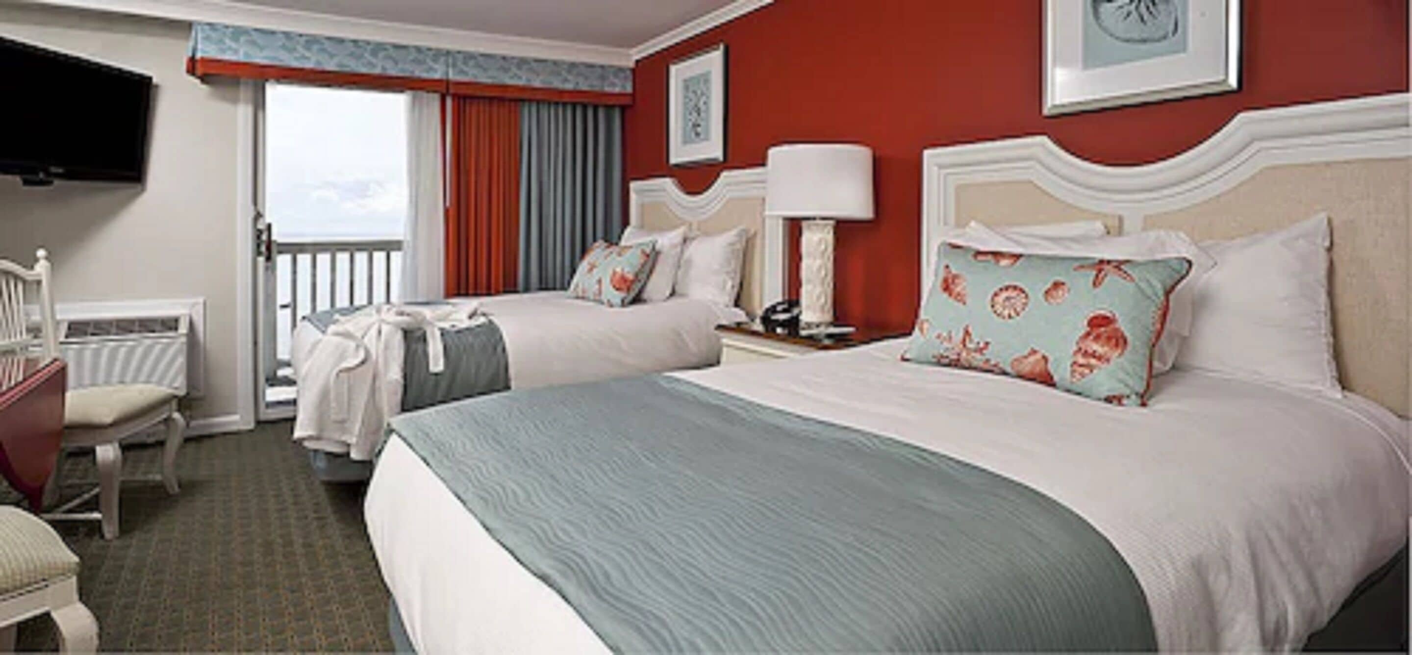A hotel room with two beds, a TV, a chair, and a balcony with curtains.