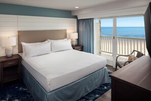 A hotel room with a large bed, two bedside tables with lamps, a chair, and a view of the ocean through a sliding glass door. - Surfside Hotel and Suites (Provincetown)