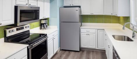 Eine moderne Küche mit weißen Schränken, einem Edelstahlkühlschrank, einer Mikrowelle, einem Backofen und einer Kaffeemaschine.