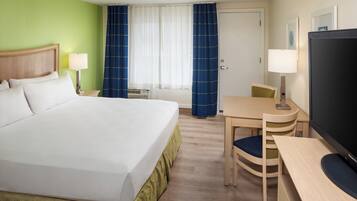 A hotel room with a bed, a desk, a chair, a television, and a window with curtains.