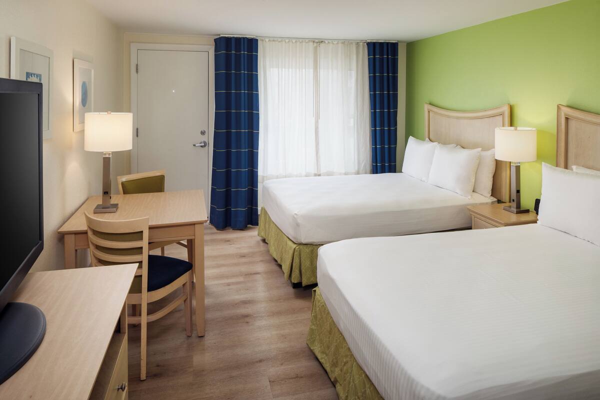 Habitación de hotel con dos camas, un escritorio, una silla y un televisor.