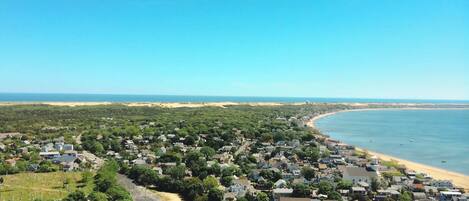 Vista aérea de uma vila costeira com uma praia, áreas residenciais e um estacionamento.