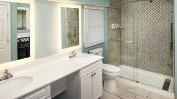 A bathroom with a double sink vanity, a toilet, and a glass-enclosed shower.