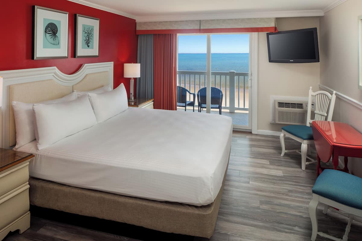 Habitación de hotel con una cama grande, televisión, escritorio con silla y balcón con vista al mar.