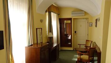 Quarto de hotel com cama, escrivaninha, cadeira e porta que dá para outro cômodo.