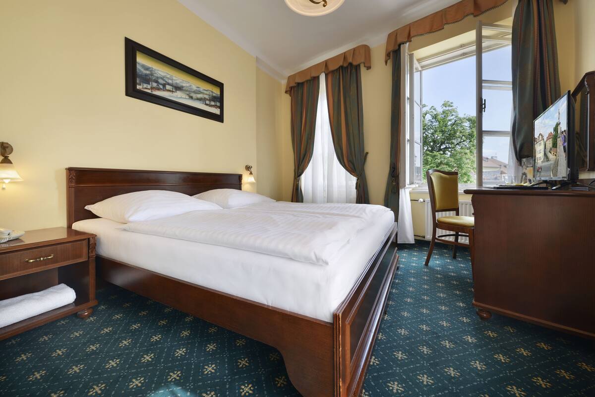 A hotel room with a large bed, a desk, a chair, a nightstand, and a window with curtains.