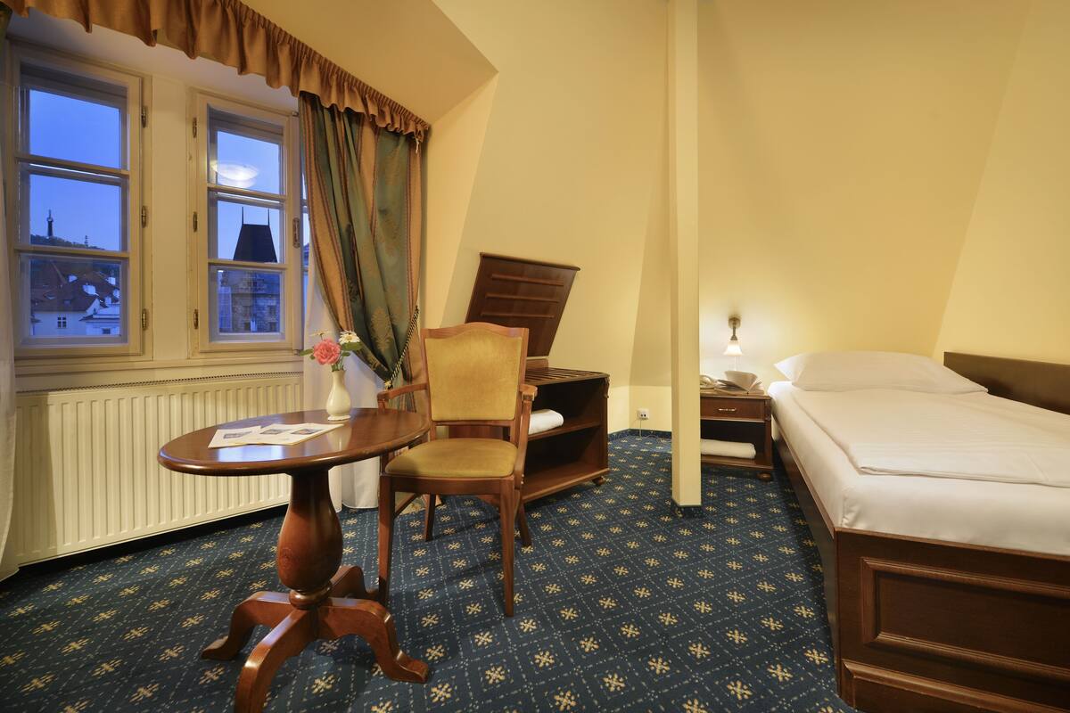 A hotel room with a bed, a chair, a small table, and a window with curtains.