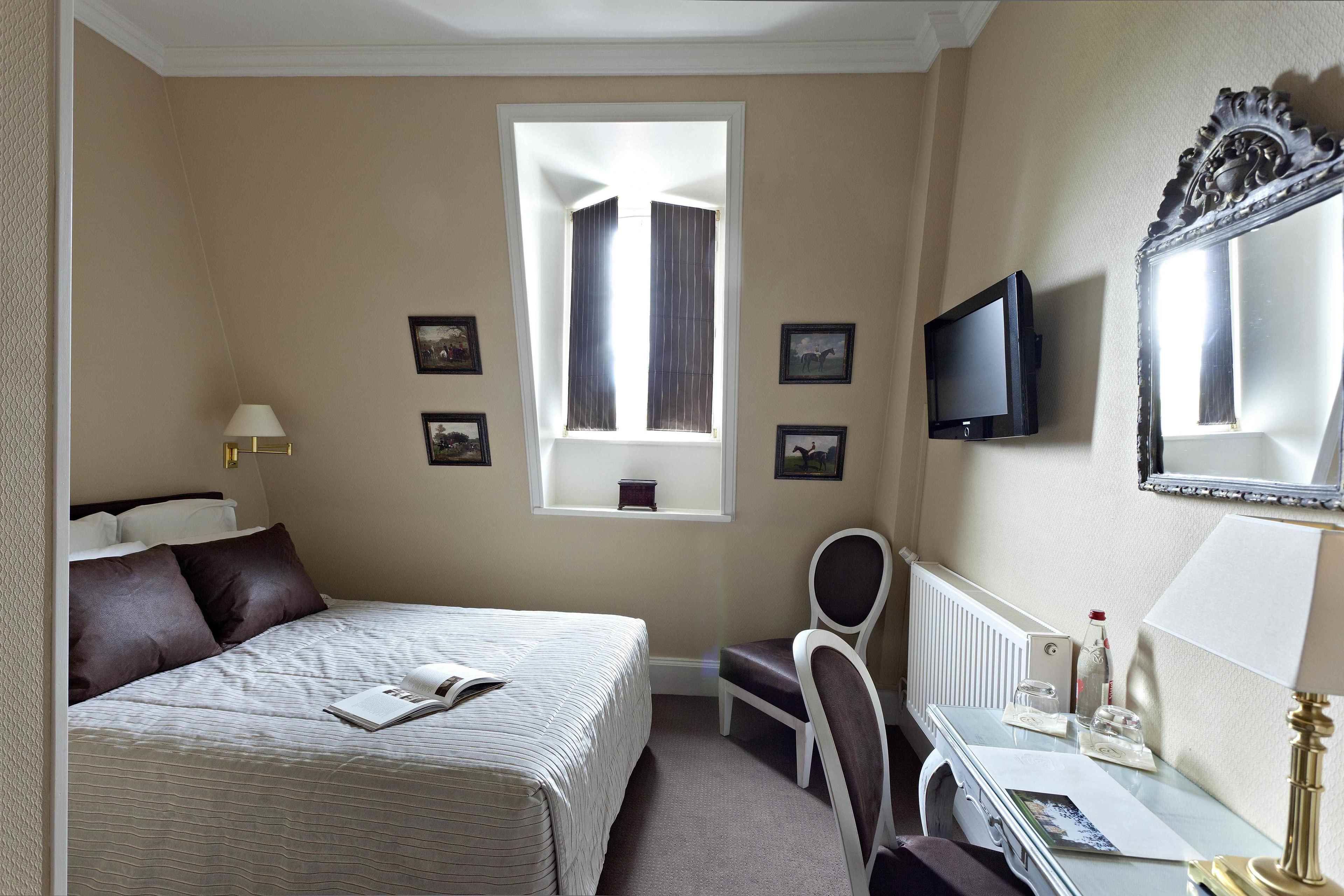 Een hotelkamer met een bed, een bureau met stoel, een televisie en een raam met gordijnen.