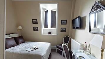 Ein Hotelzimmer mit einem Bett, einem Schreibtisch mit Stuhl, einem Fernseher und einem Fenster mit Vorhängen.