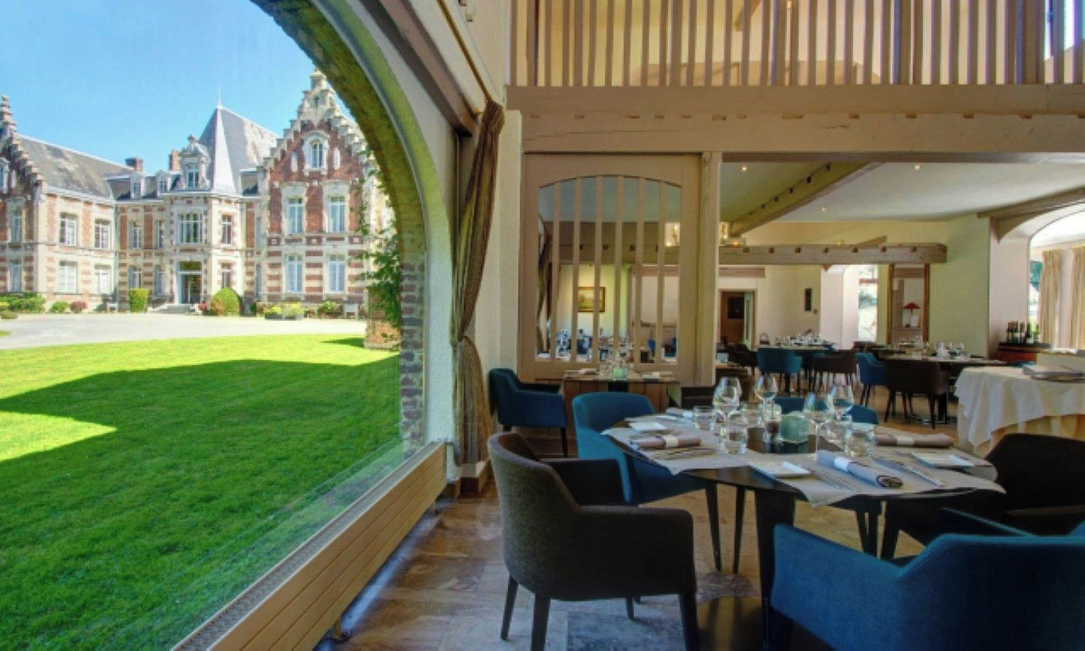 A restaurant with tables set for dining, a view of a building with a garden outside.