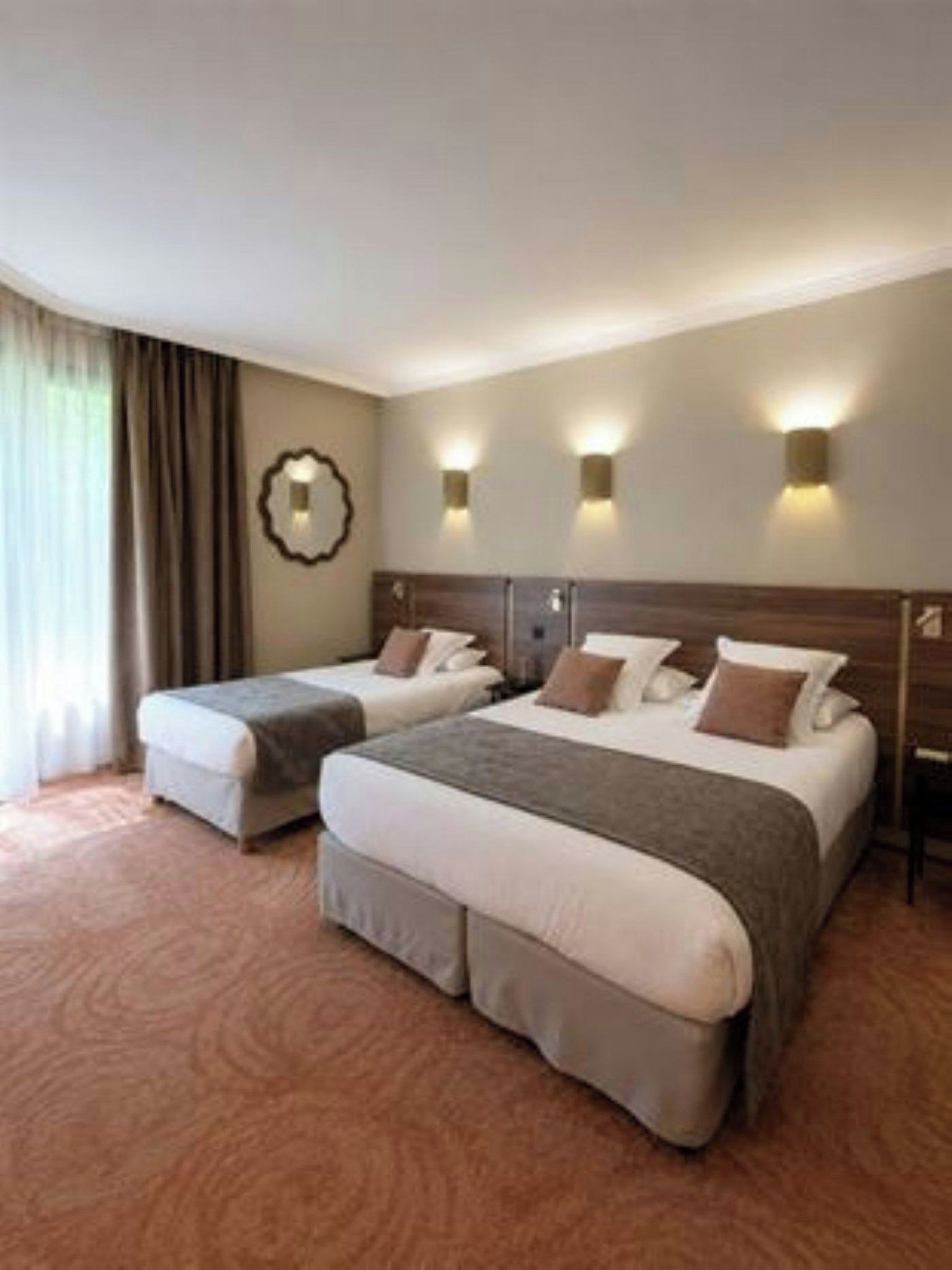 Habitación de hotel con dos camas, un ventanal con cortinas e iluminación en la pared.