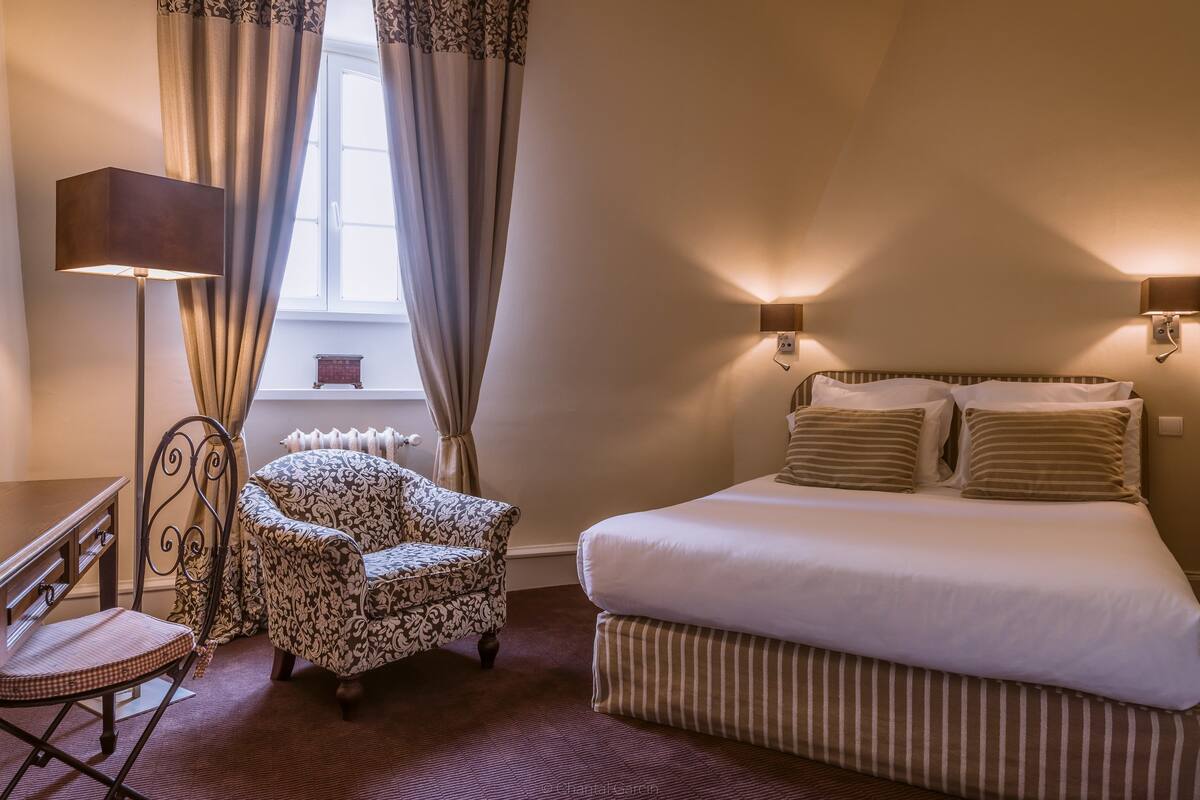 A hotel room with a bed, a chair, a desk, and a lamp.