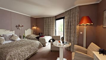 Ett hotellrum med två sängar, ett runt bord med en bärbar dator, en stol, en lampa och ett fönster med gardiner.