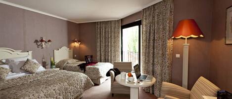 Habitación de hotel con dos camas, una mesa redonda con un portátil, una silla, una lámpara y una ventana con cortinas.