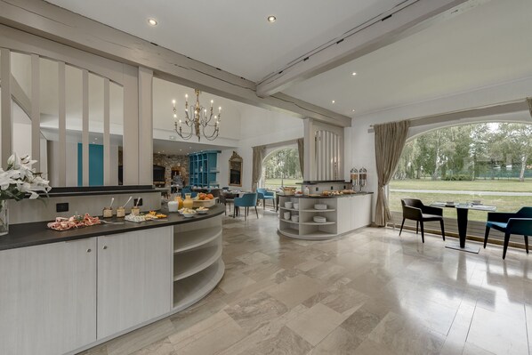 A spacious kitchen with a central island, a dining area with chairs, and a view of the outdoors. - Hôtel Château Tilques (Tilques)