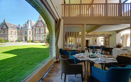 A dining area with tables set for guests, a view of a large building, and a well-maintained lawn.