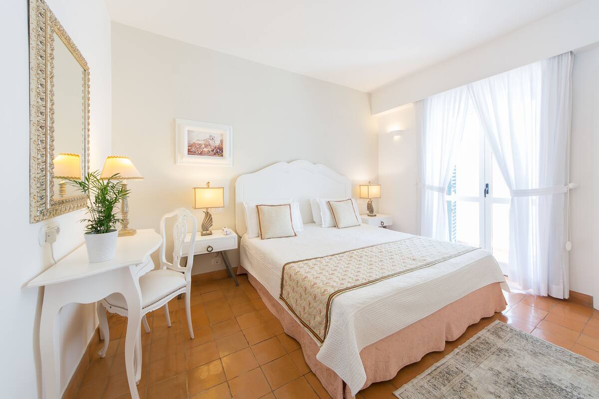 A bedroom with a large bed, a desk, a chair, and a potted plant.