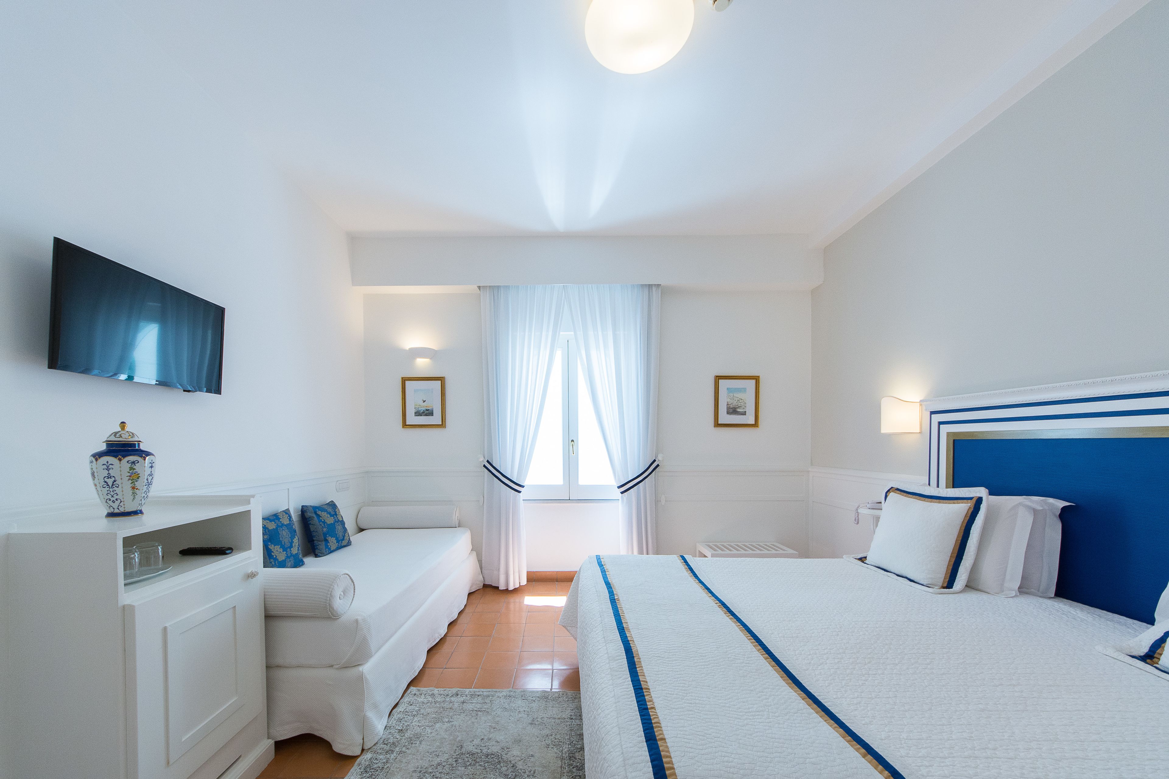 A hotel room with a bed, a bedside table, a TV mounted on the wall, and a window with curtains.
