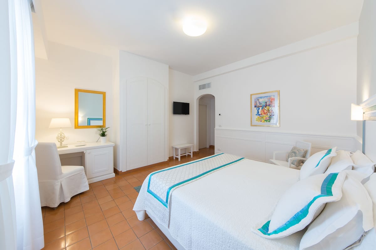 A hotel room with a bed, a desk, a chair, a TV, and a painting on the wall.